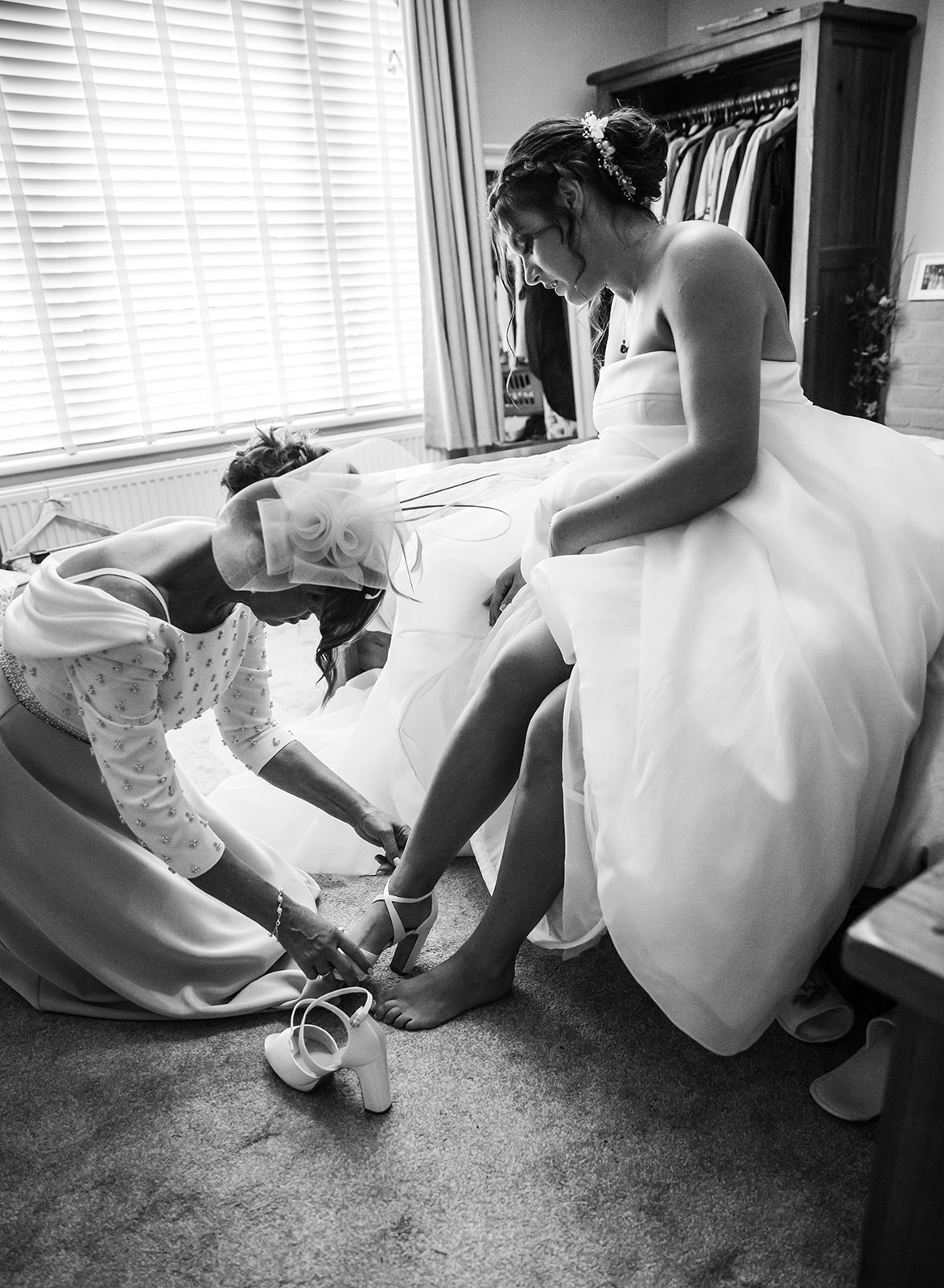 Candid black and white photograph of a mother of the bride helping the bride put on her wedding shoes during morning preparations in Gloucester.