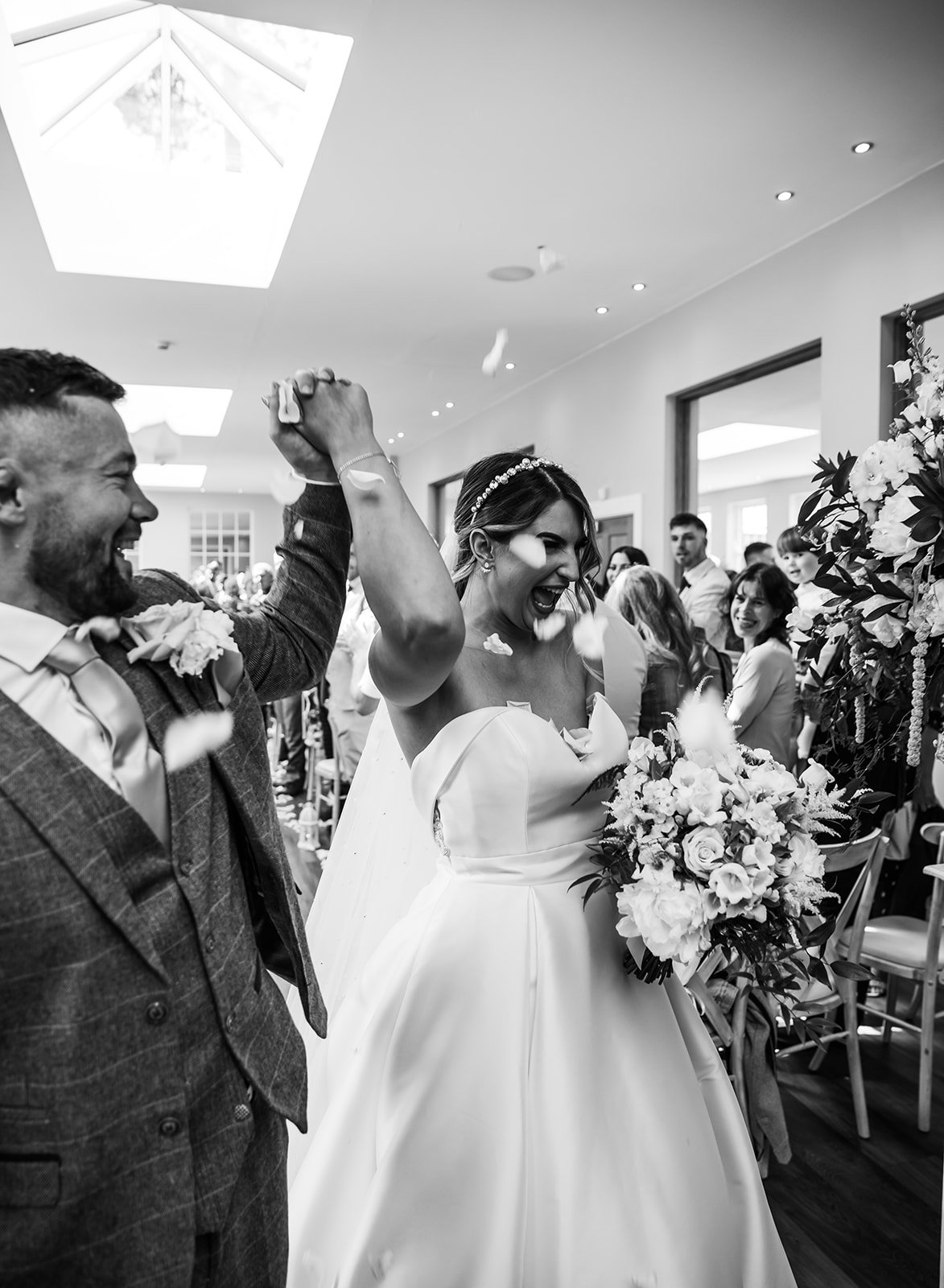 A joyful confetti exit at Bredenbury Court Barns Hereford, showing a bride and groom laughing in a bright, modern barn venue in black and white.