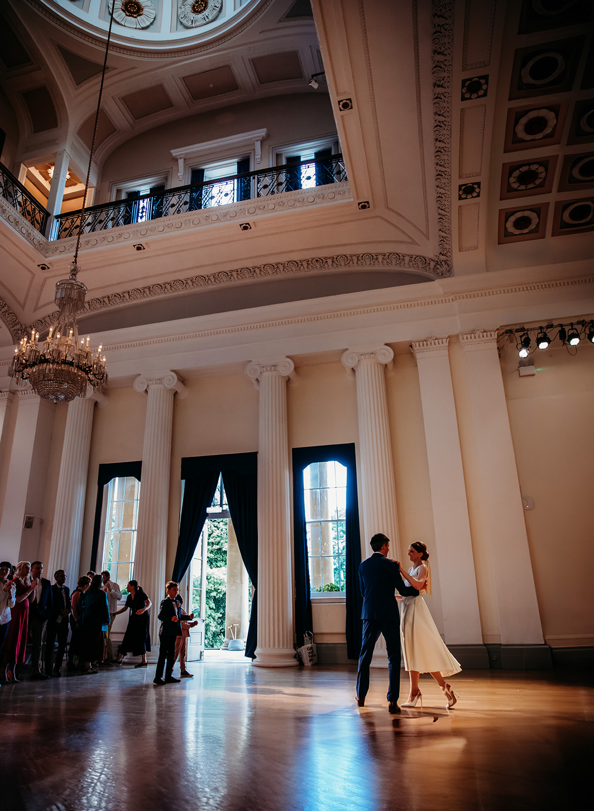 Wide-angle interior photograph of a bride and groom dancing in the grand, high-ceilinged ballroom at Pittville Pump Room Cheltenham, featuring elegant columns and historic architecture