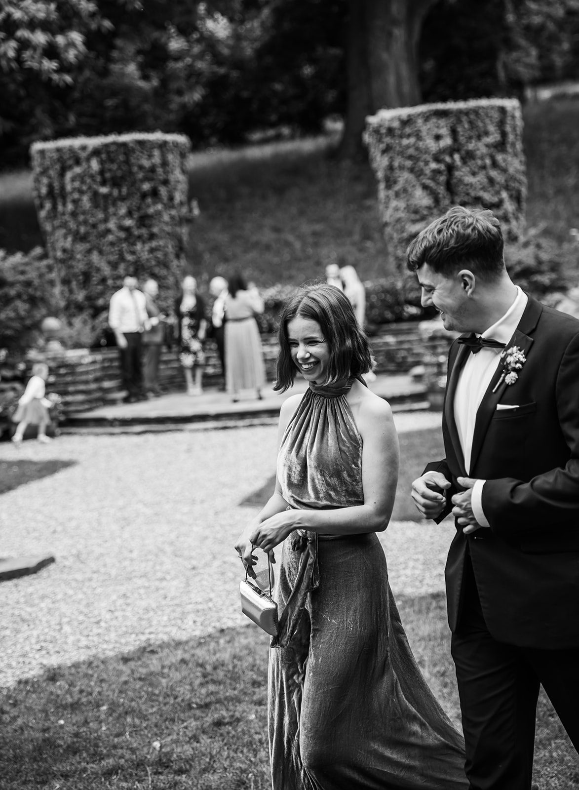 Black and white candid photography of wedding guests walking through the landscaped gardens at Coombe Lodge, Bristol.