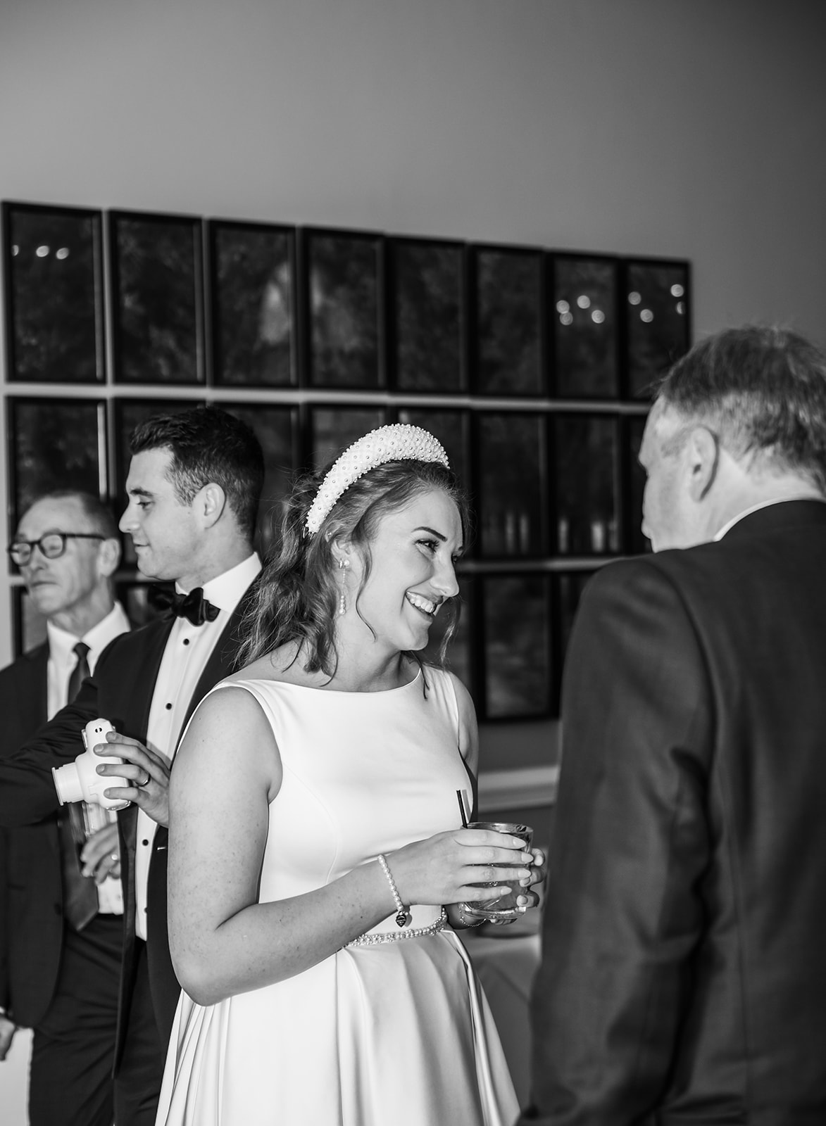 Black and white candid shot of a bride laughing with guests during a drinks reception at Queens Hotel Cheltenham, capturing a natural and relaxed wedding atmosphere.