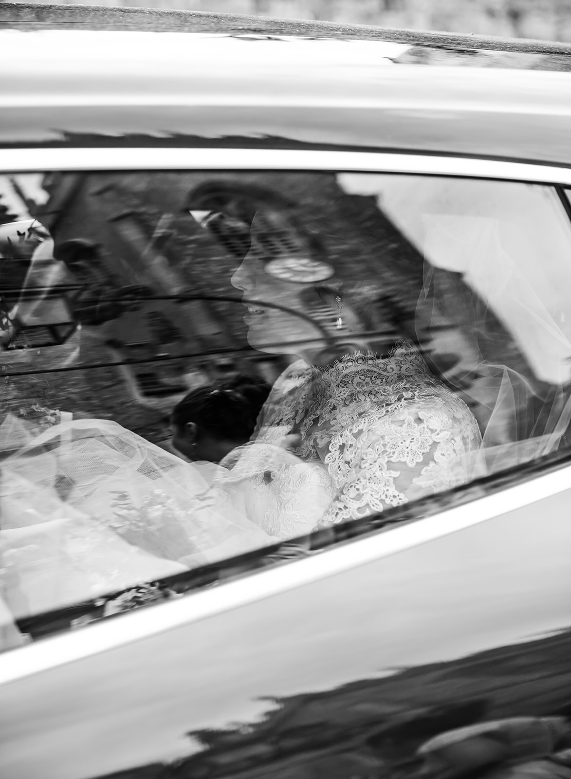 Artistic black and white photograph showing the reflection of a bride through a car window, capturing a cinematic and nostalgic wedding moment in Cheltenham.