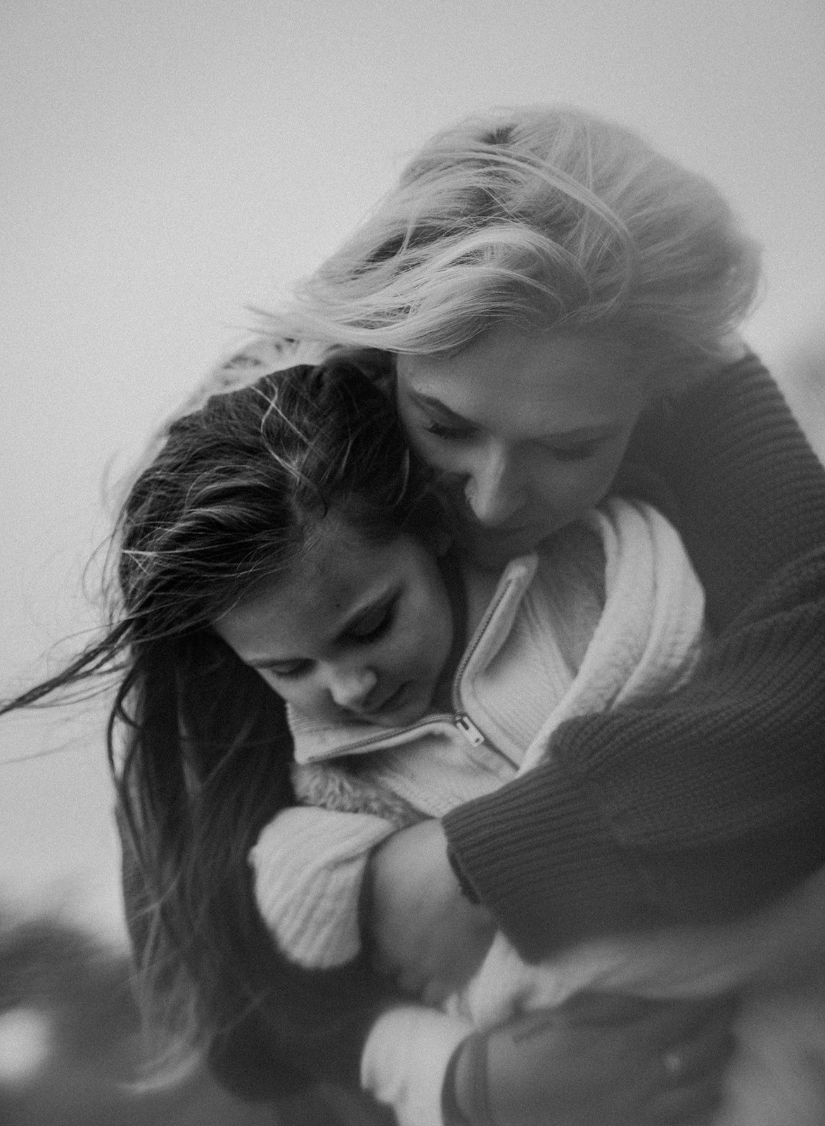 An intimate, close-up black and white photograph of a mother kissing her young daughter's forehead, capturing soft light and a cinematic, nostalgic feel.