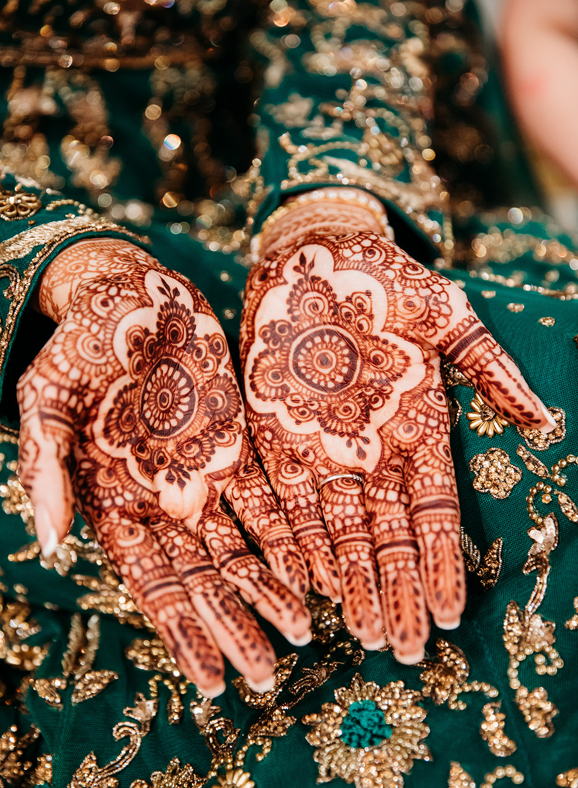 Detailed macro shot of a bride's hands featuring intricate henna or Mehndi patterns against a green and gold embroidered traditional wedding dress in Gloucestershire.