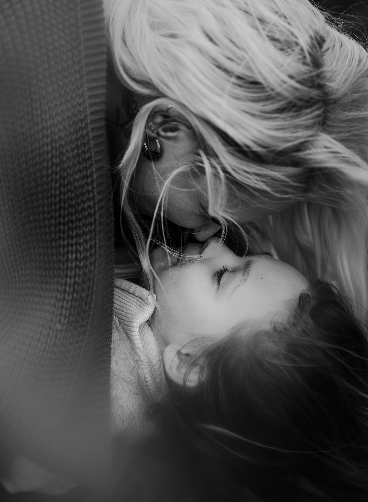 An intimate, close-up black and white photograph of a mother kissing her young daughter's forehead, capturing soft light and a cinematic, nostalgic feel.